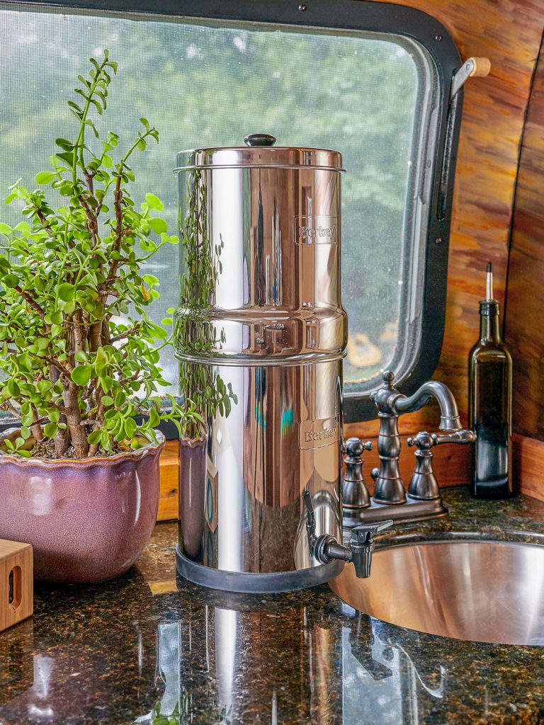 Berkey waterfilter in camper voor raam bij wasbak, plant op aanrecht
